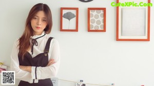 A woman in a white shirt and black overalls posing for a picture.
