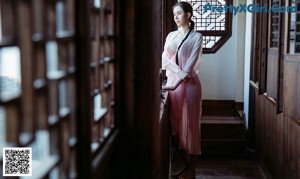 A woman in a white robe standing by a window.
