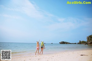 Two women in bikinis are posing for a picture on the beach.