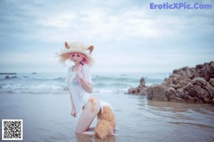 A woman with pink hair sitting on a rock by the ocean.