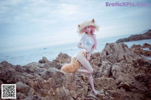 A woman in a white dress and a straw hat on a beach.