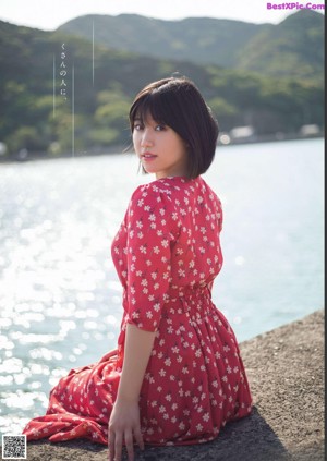 A woman in a red dress sitting by the water.