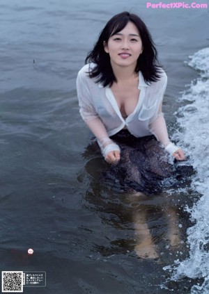 A naked asian woman sitting in a bathtub next to a window.