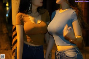 A woman in a blue shirt and jeans is kissing another woman.