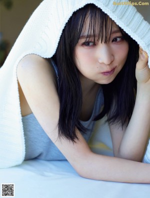 A woman sitting on a bed in a blue and white striped shirt.