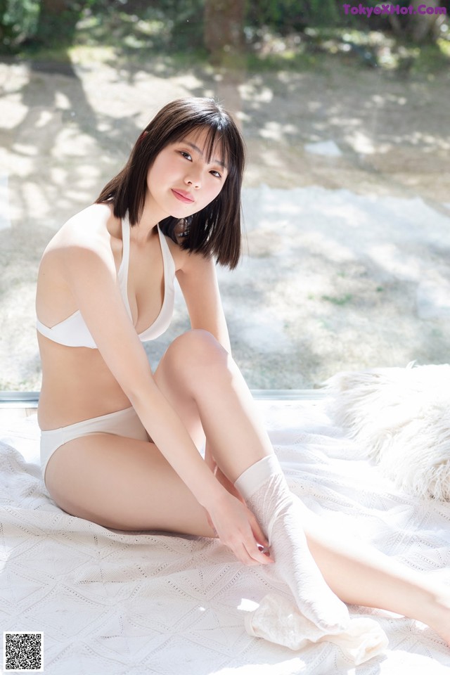 A woman in a white bikini sitting on a bed.