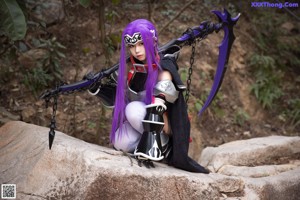 A woman with purple hair sitting on a rock.