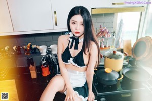 A woman in a maid outfit posing in a kitchen.