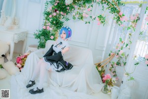A woman dressed in a maid outfit standing in front of flowers.