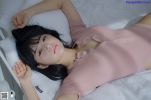 A woman in a pink bodysuit standing on a bed.