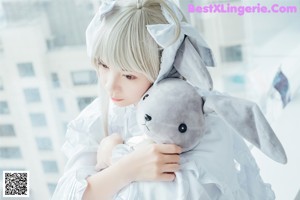 A woman in a white dress holding a teddy bear.