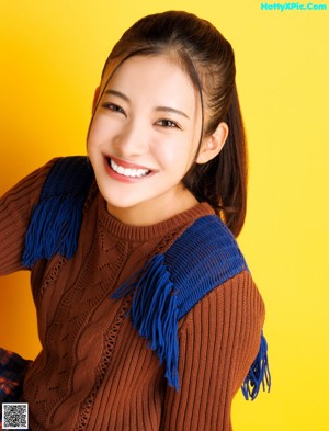 A woman in a brown sweater and plaid skirt posing for a picture.