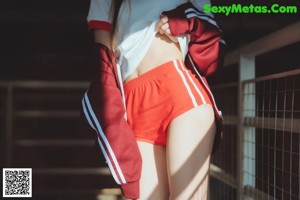 A woman in a white shirt and red shorts sitting on a wooden floor.