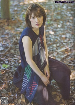 A woman sitting on the ground in the woods.