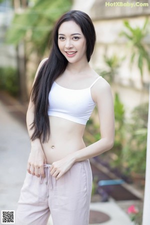 A woman in a white top and pink pants sitting on a ledge.