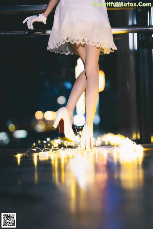 A woman in a white dress and high heels standing on a railing.