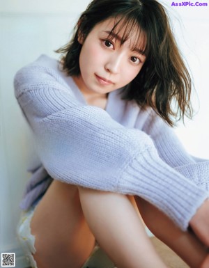 A woman sitting on a green couch wearing a white sweater and daisy skirt.