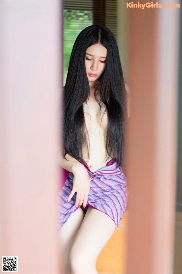 A woman with long black hair sitting on a window sill.