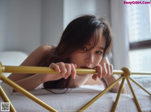 A woman in a white bodysuit sitting on a bed.