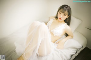 A woman sitting on a bed wearing a white lingerie.